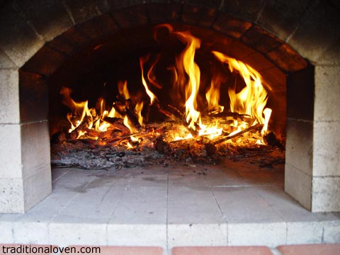 Photo of brick oven dome being heated up by wood fire.