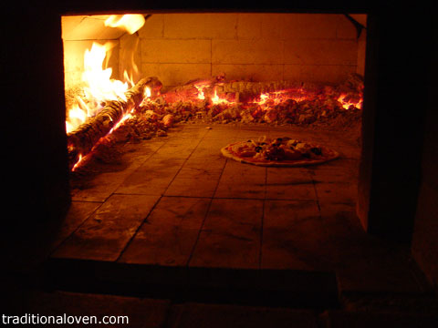 Picture of pizza placed directly onto wood oven's hot firebrick dome.