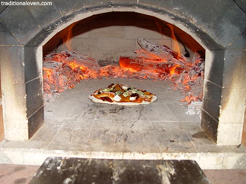Picture of wood fire red hot cinders and making pizza among them.