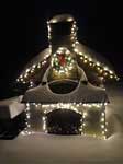 The oven with Christmas lights on, other Christmas decorations on the oven and covered by snow outside.